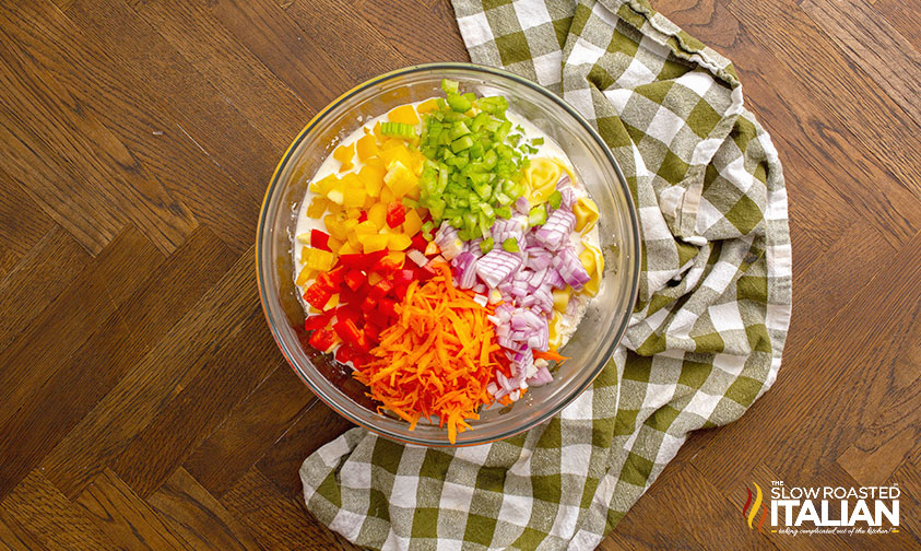 rainbow of chopped veggies over tortellini and dressing in bowl