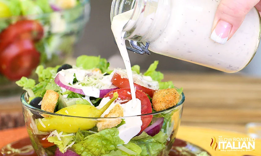 pouring creamy italian dressing over salad