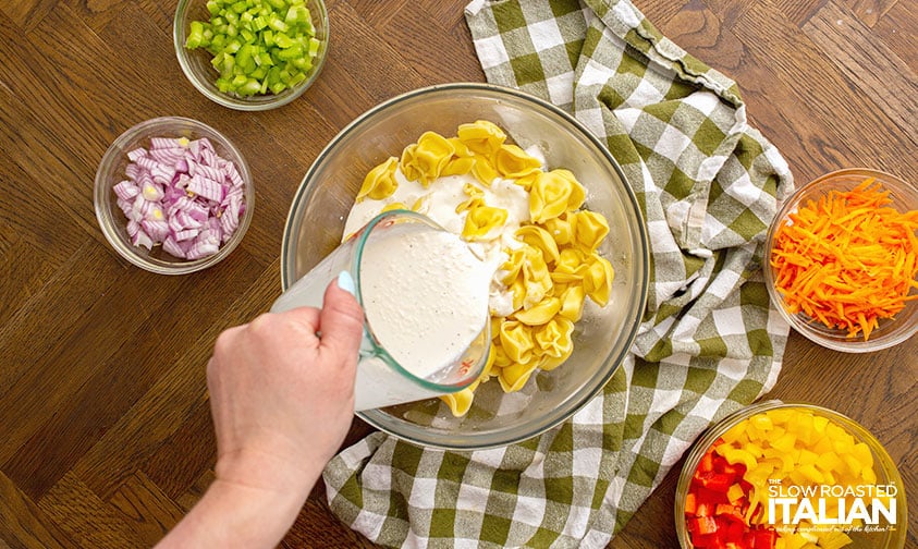 pouring creamy dressing over cooked tortellini