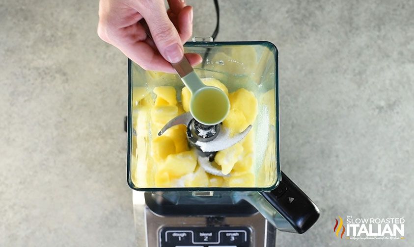 citrus juice in measuring spoon over blender with pineapple whip ingredients