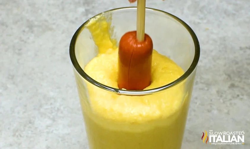 dipping hot dog on a stick into tall glass of cornmeal batter