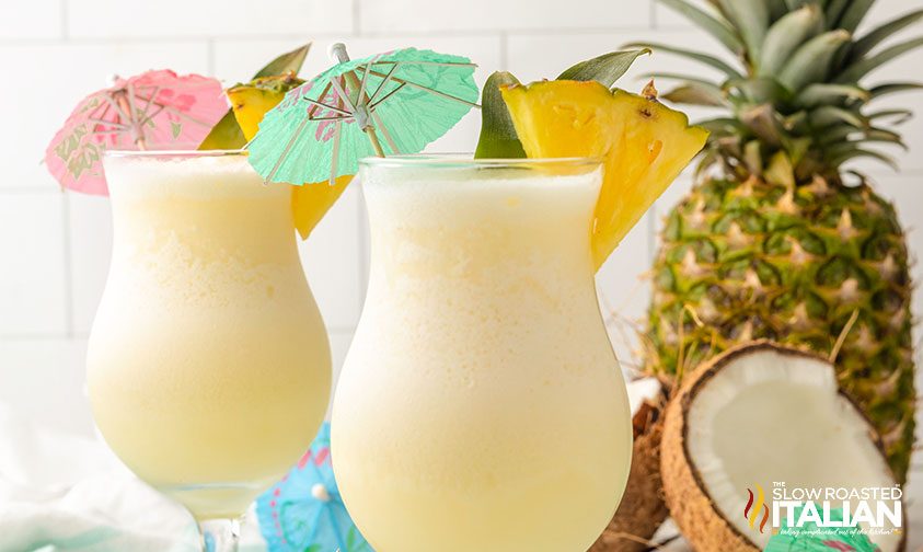 pina colada drink in hurricane glasses with umbrella and fruit garnishes