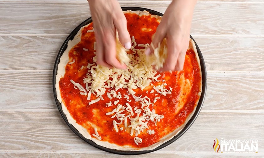 sprinkling shredded cheese over marinara topped pizza dough