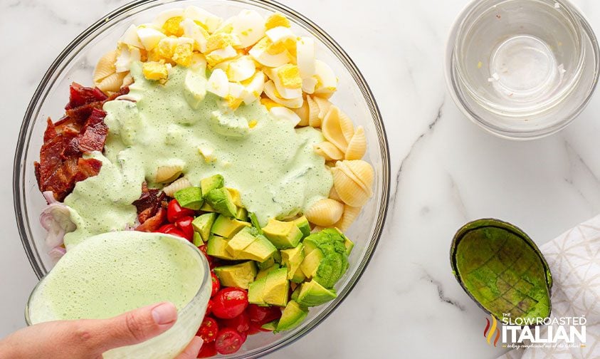 pouring green goddess dressing over bowl of ingredients