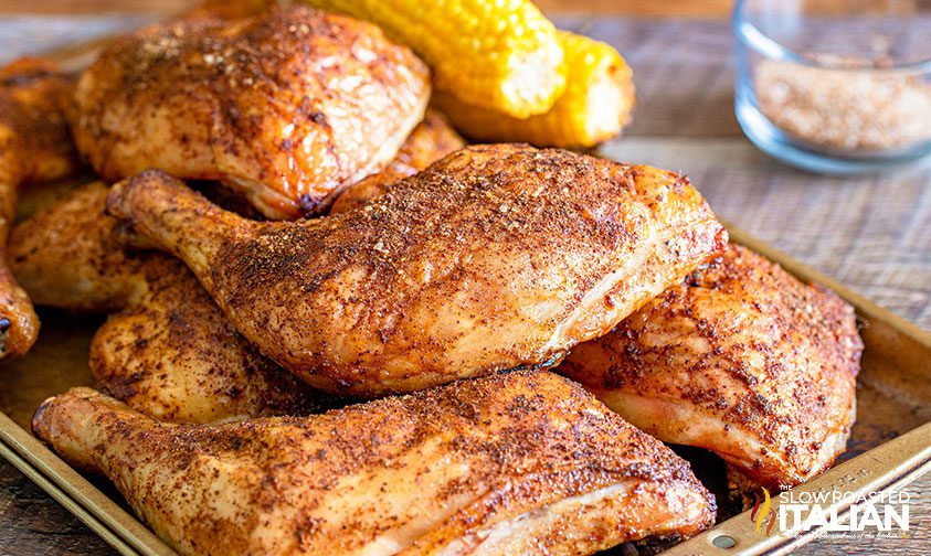 smoked chicken quarters stacked on pan with corn on the cob