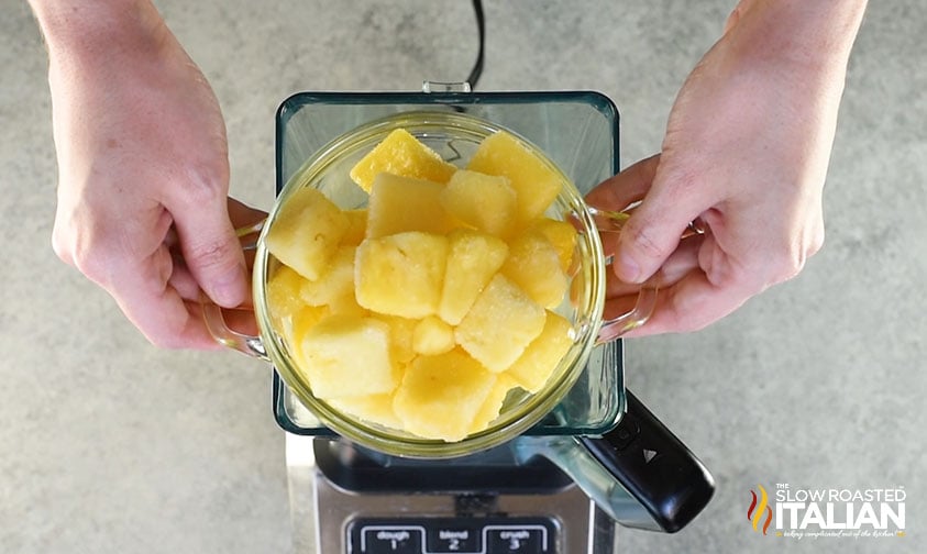 holding bowl of frozen pineapple over blender