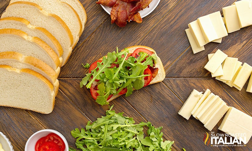 arugula and sliced tomato added to bacon and cheese on bread