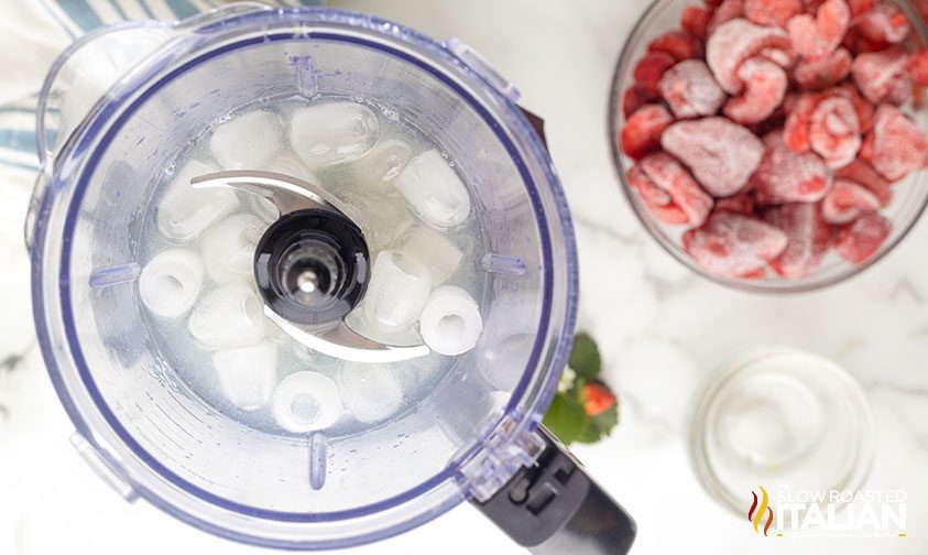 bowl of frozen strawberries next to blender with ice and liquid inside