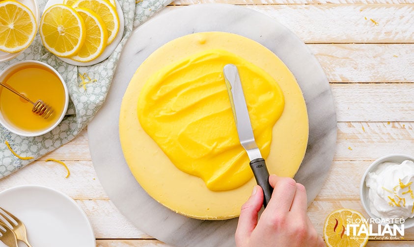 spreading lemon curd on top of baked lemon cheesecake