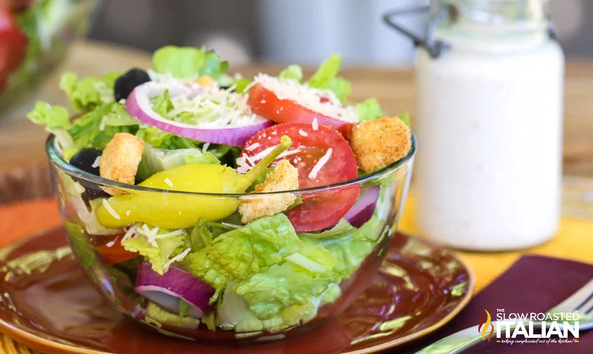 bowl of olive garden salad with bottle of dressing in background