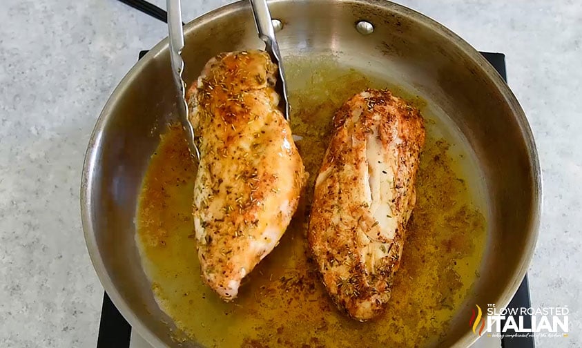 placing seasoned chicken breasts in skillet with tongs