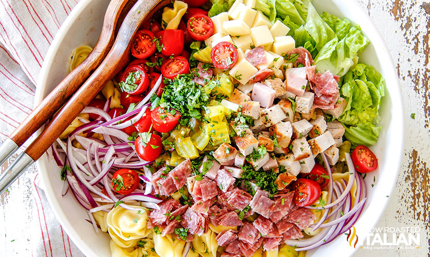 tortellini pasta salad topped with meat, cheese, and veggies in a large bowl