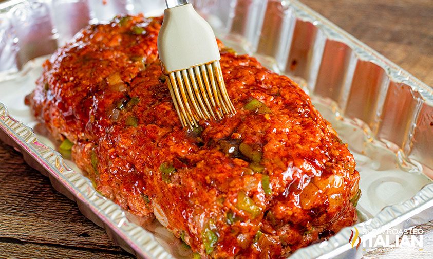 brushing bbq sauce glaze over uncooked meatloaf