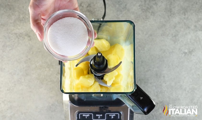 adding sugar to blender with pineapple and coconut milk