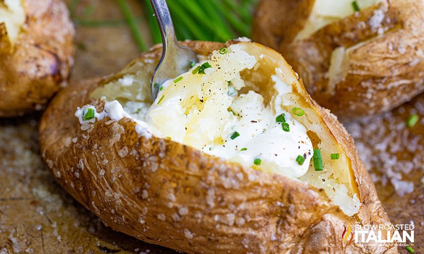 scooping out center of baked potato with sour cream and chives