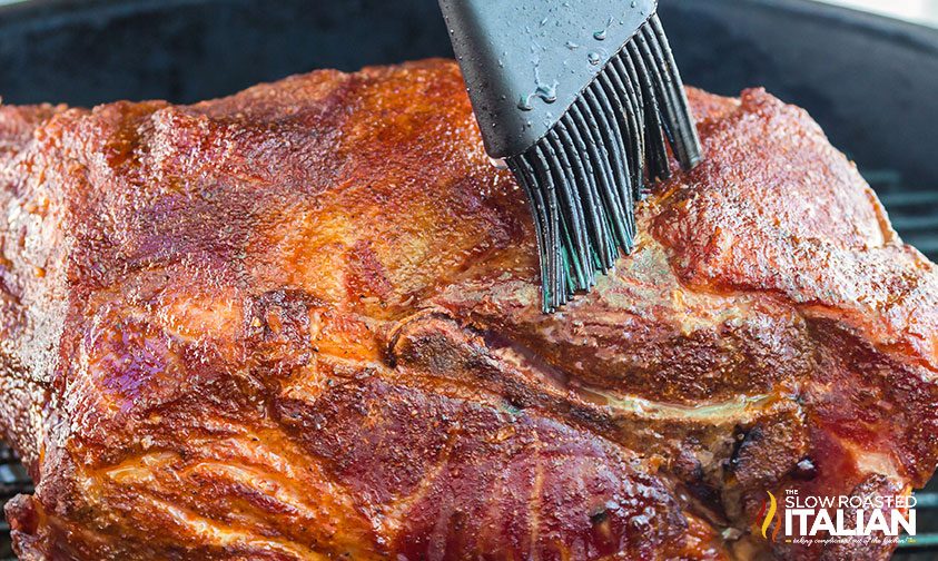 close up: brushing liquid over pork butt on smoker