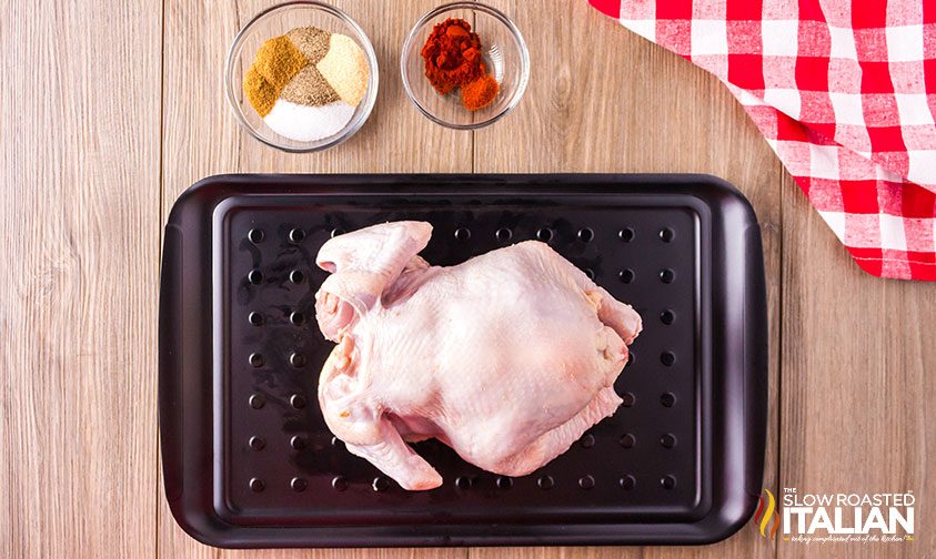 raw whole chicken on metal tray next to bowls of spices