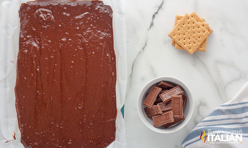 parchment lined pan of brownie batter next to graham crackers and chocolate bar pieces