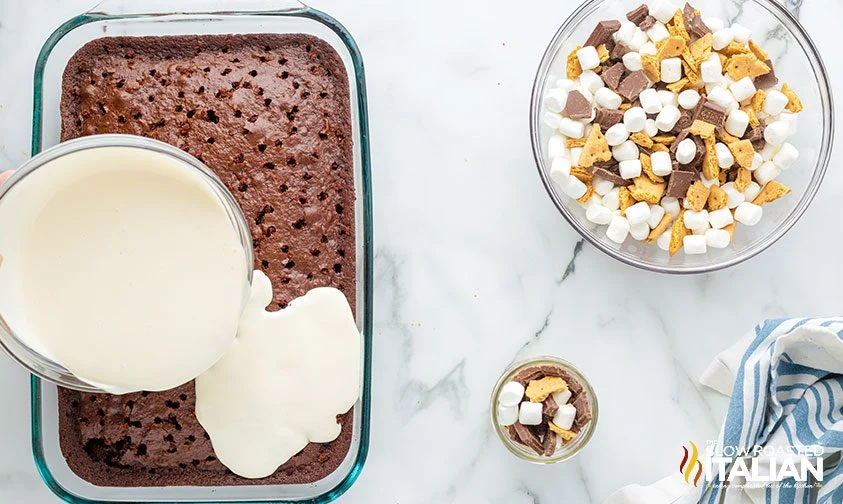 pouring marshmallow topping over chocolate poke cake