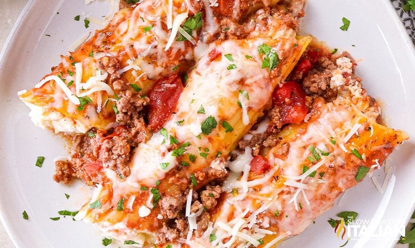 three stuffed manicotti with sauce and cheese on plate