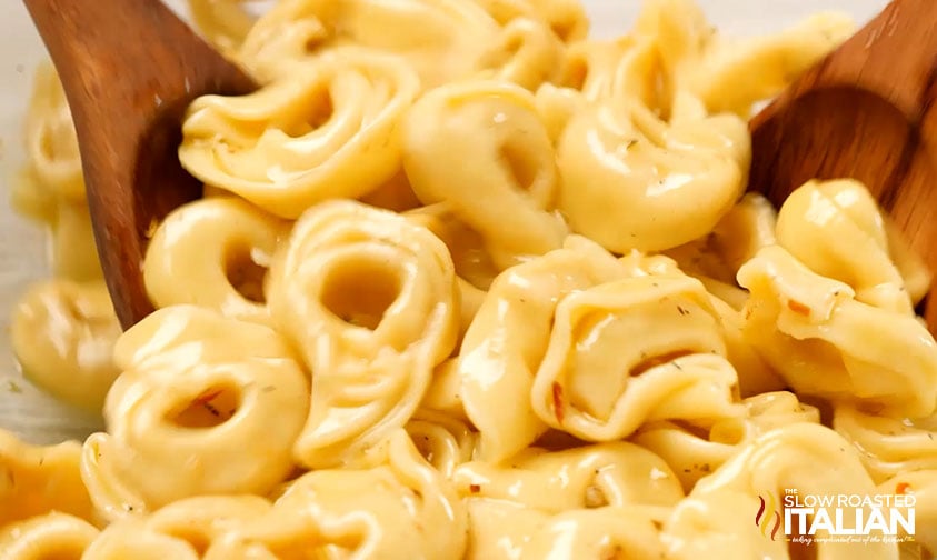 tossing cooked tortellini in dressing