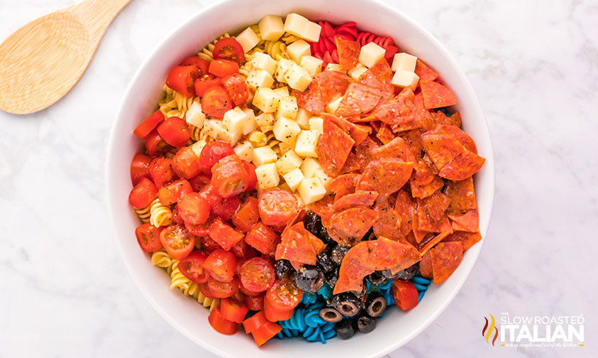 pepperoni, veggies, and cheese in a bowl with tri color pasta