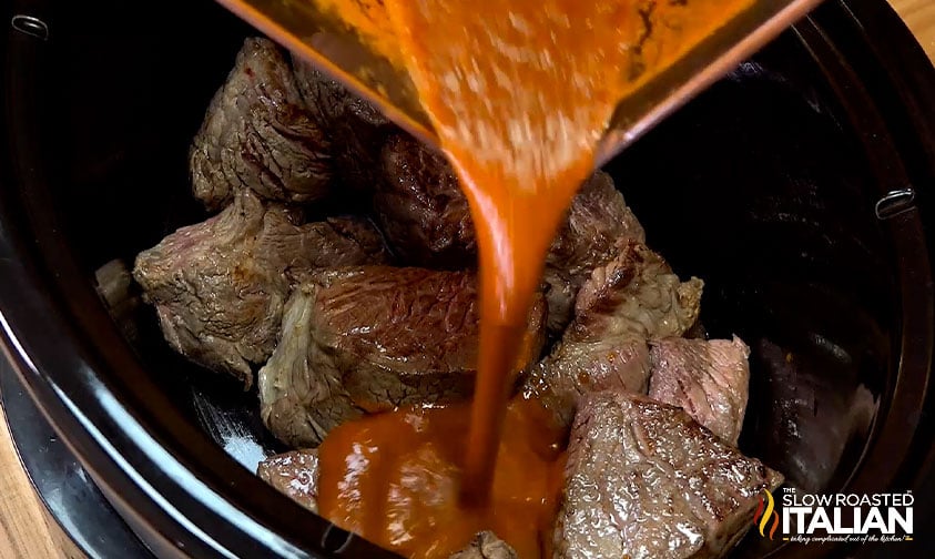 pouring sauce over beef in crockpot