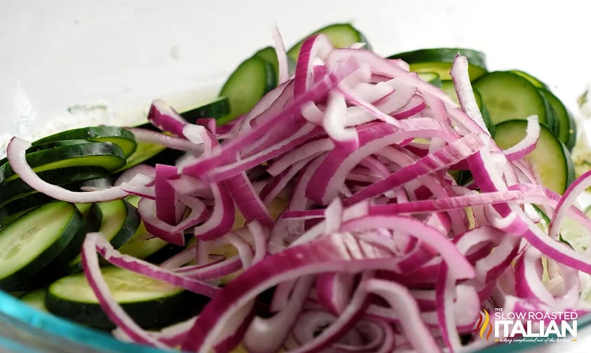 slices of red onion in a glass bowl with sliced cucumber