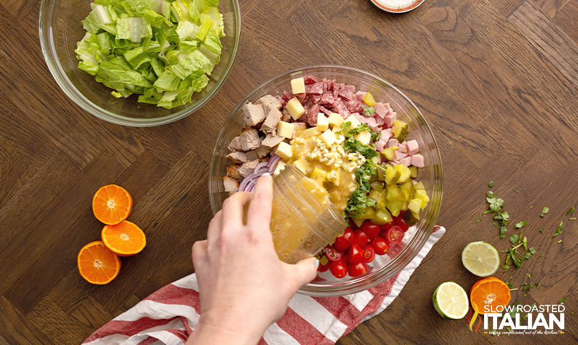pouring dressing over cuban sandwich pasta salad