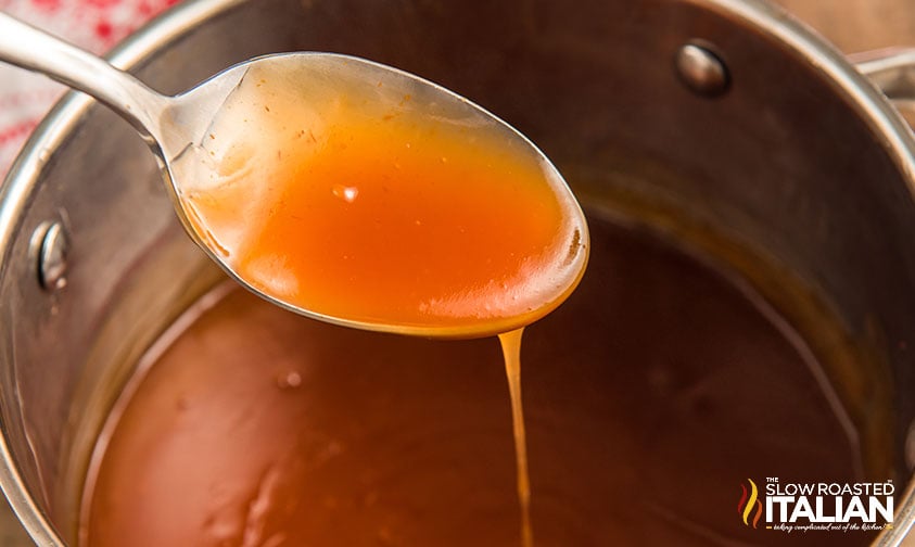 sweet and sour sauce on a spoon over a large pot of sauce