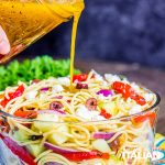 pouring dressing on greek spaghetti salad