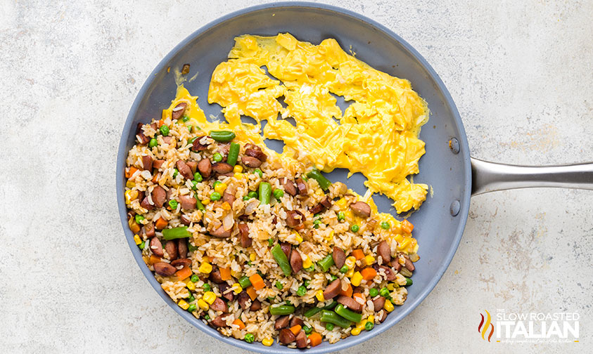 adding scrambled eggs to skillet of hot dog fried rice