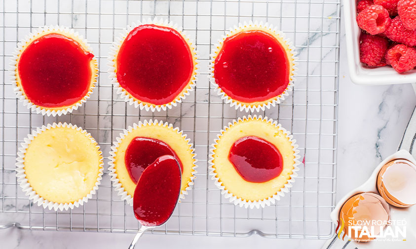 spooning raspberry sauce on top of cheesecakes