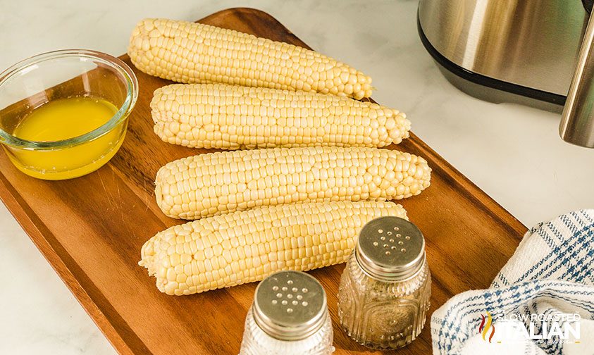 freshly shucked corn with salt and pepper shakers and bowl of melted butter
