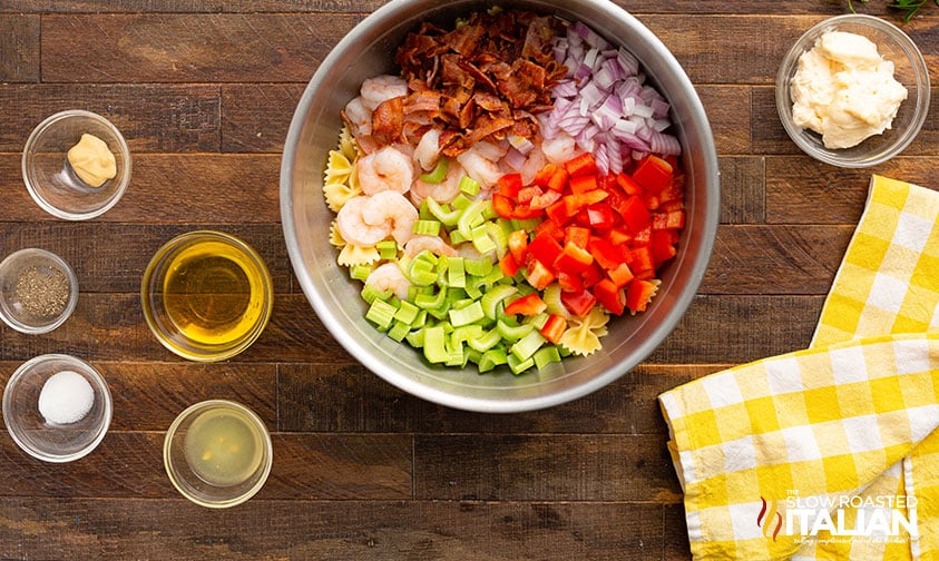 pasta, bacon, veggies, and shrimp in bowl surrounded by dressing ingredients