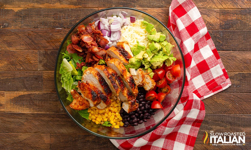 sliced chicken, bacon, veggies, and beans over lettuce in bowl