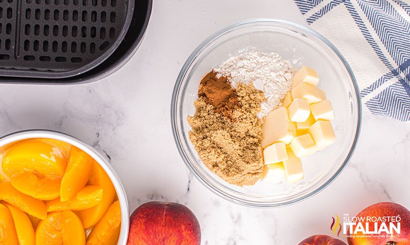 crisp topping ingredients in a bowl next to another bowl of canned peaches