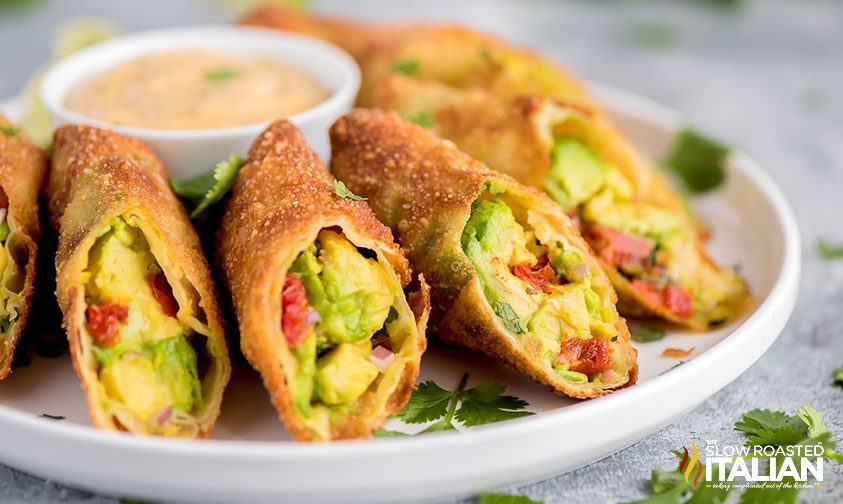 diagonally sliced avocado egg rolls on plate with dip