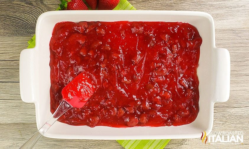 spreading canned pie filling into a baking dish with a spatula