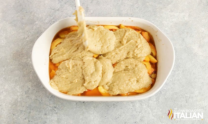 spooning cobbler dough over spiced peaches in baking dish
