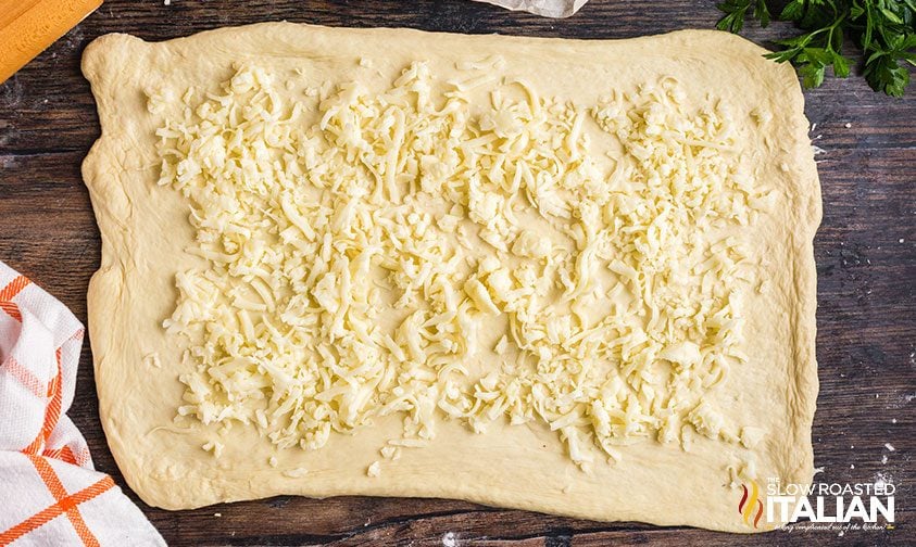 layer of shredded cheese on rolled out pizza dough