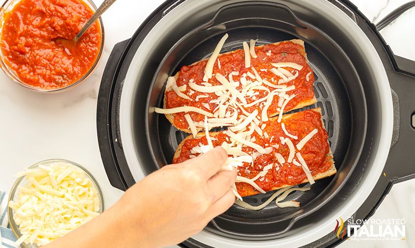 sprinkling shredded mozzarella on french bread pizza in air fryer