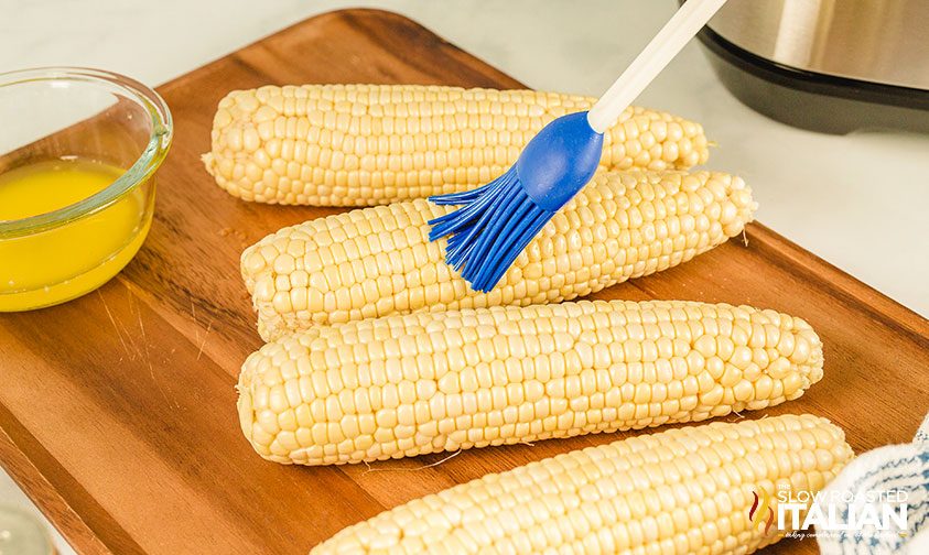 brushing melted butter onto ears of corn with basting brush