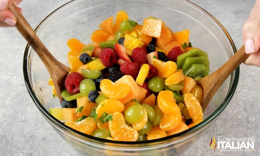tossing fruit salad with oranges in bowl