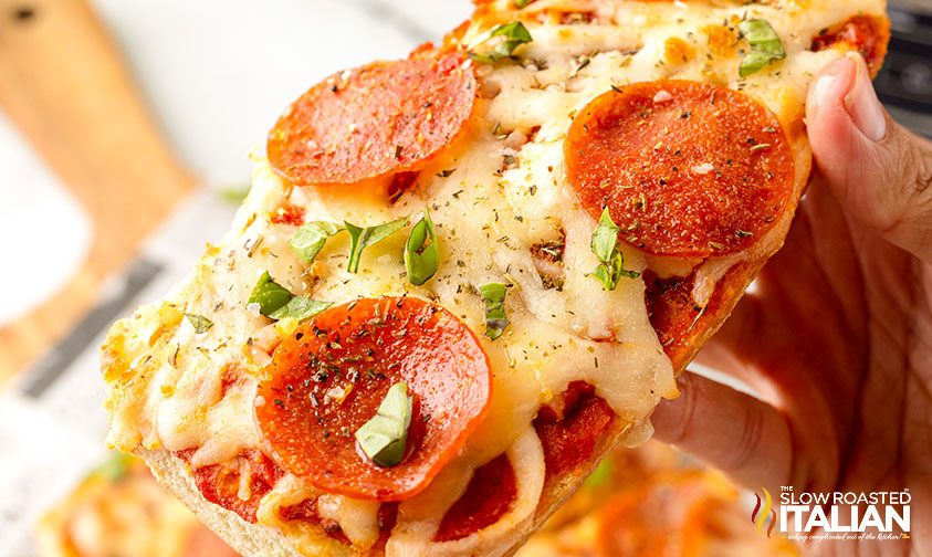 close up: holding french bread pizza with pepperoni and spices