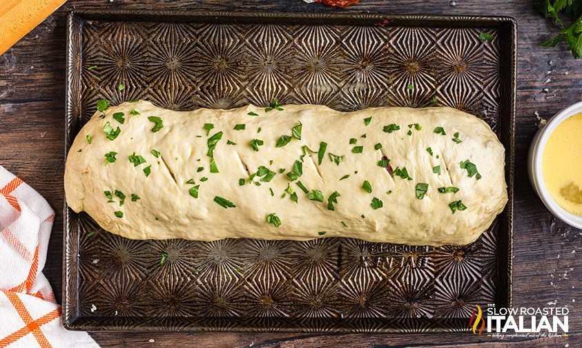 uncooked stromboli topped with fresh parsley on baking sheet