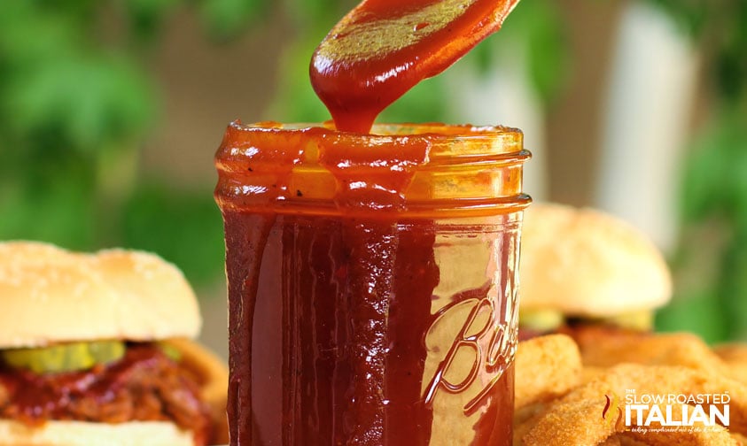 spooning bbq sauce out of jar with some dripping down the sides