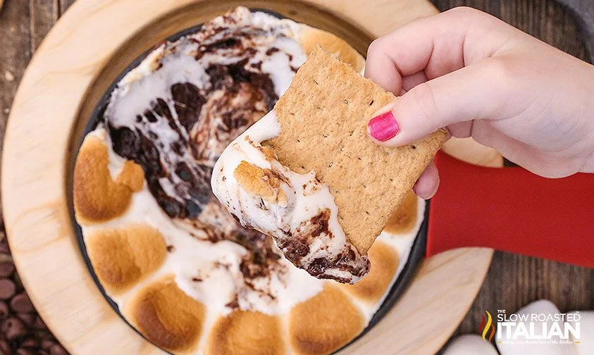 holding graham cracker with chocolate marshmallow dip
