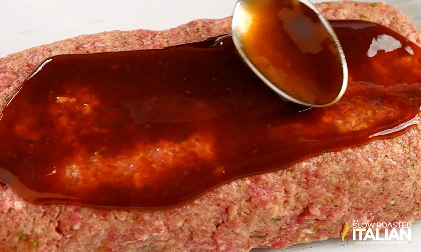 spreading glaze on uncooked meatloaf with spoon