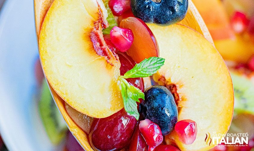 closeup: fruit salad with peaches on a wooden spoon